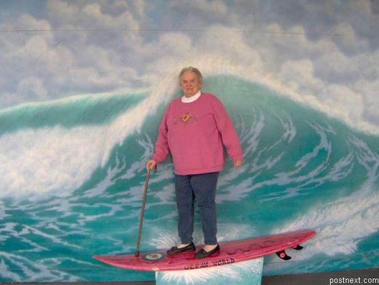 Una señora en tierra firme subida en una tabla de surf con una foto de una ola