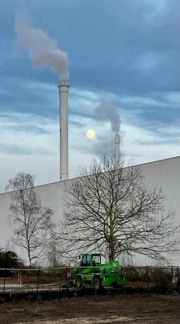 Das Bild zeigt eine Fabriklandschaft an einem trüben Tag. Im Hintergrund erheben sich zwei hohe, weiße Schornsteine, aus denen Rauch aufsteigt, dazwischen steht der Mond. Davor befindet sich eine lange, weiße Fabrikhalle. Im Vordergrund steht ein grünes Baufahrzeug auf einem unbefestigten Gelände. Einige kahle Bäume sind ebenfalls im Bild zu sehen, die sich vor der Fabrikhalle abheben. Der Himmel ist bewölkt und grau.
Bereitgestellt von @altbot, generiert mit Gemini