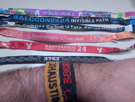 wristbands for
hack mas castle
balccon 2024
campp 2024
emf2024
easterhegg 2024
37c3
on a table. below that an arm with the 36c3 and 38c3 wristband still on it.