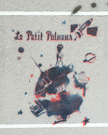 Pochoir sur un mur en ciment, représentant le petit prince (surtitré le petit pol[l]ueur) sur une planète en partie cassée, avec des cratères, un missile "police"
