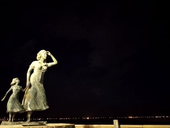 Photo d’une statue en bronze de plus de 2 m de haut, installée au bout du môle du Grau Du Roi, face à la mer Méditerranée 
Une femme scrute l’horizon en tenant sa fille par la main en attendant le retour des bateaux de pêche.