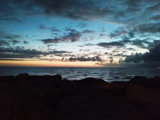 Photo plan large du soleil partant â l’ouest 
Vue sur la Méditerranée à perte de vue
Au premier plan les derniers rochers du môle du Grau Du Roi 
Le ciel est jaune, orange, rose, violet avec  quelques nuages qui parsèment le ciel. 
Le vent, les embruns… tout est calme.