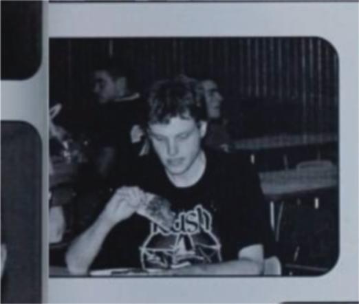 A monochrome picture of me taken candidly my senior year. I'm not aware of the photo being taken and am looking glumly at a slice of pizza. I am wearing, appropriately, a Rush T-shirt from the 30th anniversary tour because it was an out of uniform day. I am completely alone at my table.