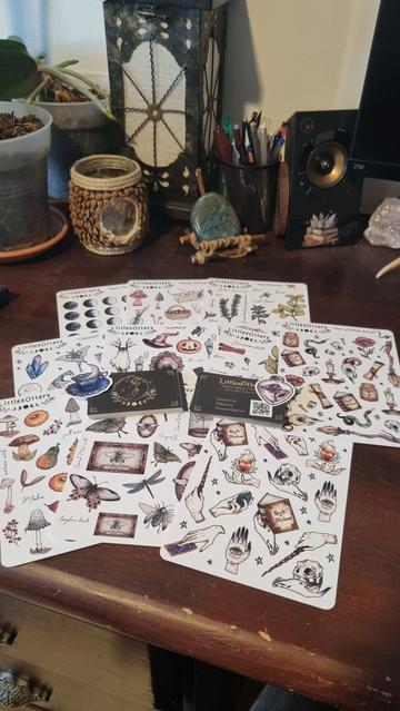Some witchy stickers on different pages and the business cards from their maker. Some pages are full of mushrooms, others insects, magical objects... They're on a working desk with crystals and plants.
❉
Quelques autocollants witchy sur différentes planches et les cartes de visite de leur créatrice. Certaines planches sont pleines de champignons, d'autres d'insectes, d'objets magiques... Elles sont sur un bureau avec des cristaux et des plantes.