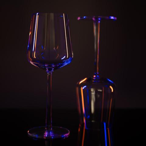 The image shows two wine glasses, one upright and the other upside down, on a reflective surface. They are illuminated with colored lighting that creates a mix of blue, purple, and orange reflections on the glass surfaces.