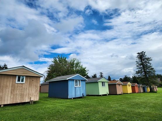 Colorful cabins lined in row under a cloudy sky with breaks of blue.