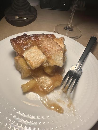 Slice of apple pie & fork on a white plate.