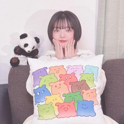 Fuuka touching her chin with a pillow on her lap with a panda plush on the couch.