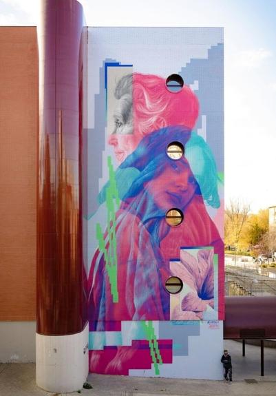 Streetartwall. A colorful mural with two women was sprayed/painted on the outside wall of a four-story (19,5 x 7 Meters) modern building with small round windows. The mural is very unusual and designed in different pastel colors. The depiction of an elderly lady and a young girl overlap semi-transparently. The older lady is looking to the left and is depicted in pink. Only her face is kept colorless in shades of grey. A young girl with brown hair is leaning on her shoulder and looking towards the viewer. Her colors are pink and blue. The colors overlap and are disturbed by neon green graffiti lines. Blue skyscrapers are painted in the background and a bright rectangle in the corner shows a pink orchid. A beautiful and harmonious arrangement that conveys a sense of family, conversation and closeness. (In the photo, the artist is standing at a corner of the house.)