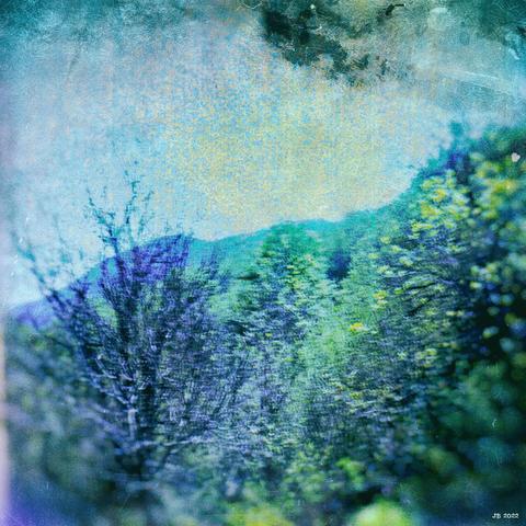 Farbfoto mit psychedelischen Farben im Bereich grün-blau-violett. Blick über Laubbäume auf einen Bergzug und den Himmel in den italienischen Abruzzen. Seagull 4A mit einem Defekt auf Fuji Provia-Diafilm.