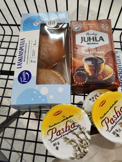 Kuvassa pakkaus jossa 2 laskiaispullaa, paketti kahvia ja muutama purkki pashaa kauppakärryssä