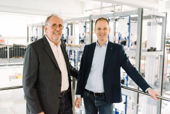 Zwei Männer stehen an einem Geländer. Im Hintergrund ist eine Sanitärtechnische Anlage zu sehen. 24. Sanitärtechnisches Symposium 2025. Abschied von Prof. Schmickler.