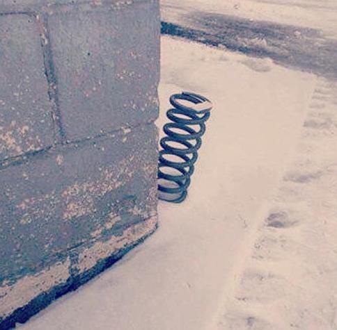 A car spring, peeking around the side of a block wall on snowy ground