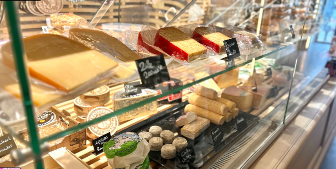 Photo shows a part of a deli-shop , with showcase filled with Mediterrane cheeses , hams and sausages.