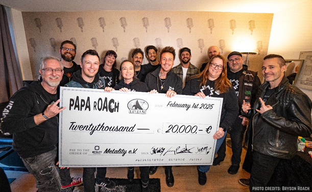 offizielles Pressebild von der Spendenübergabe von Papa Roach an Metality. Im Bild sind die Bandmitglieder von Papa Rocha und Member des Metality e.V. Sie halten einen großen  Spendenscheck in die Kamera.