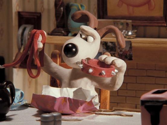 A white dog with a black nose and brown ears looks skeptically at the present he's just unwrapped, a red dog collar with spikes and a matching leash.