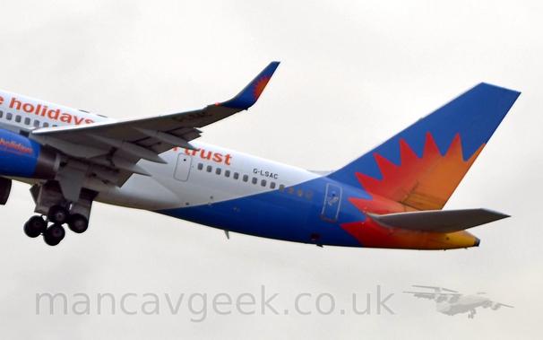 Closeup of the blue tail and rear fuselage of a white, twin engined jet airliner flying from left to right at a low altitude, with the undercarriage being retracted, flaps extended from the rear of the wings, and the nose raised significantly, suggesting it has just taken off..
There is a red, orange, and yellow sunburst at the lower rear of the tail, stretching over the rear fuselage.
This same sunburst is repeated on the blue upturned wingtips.
The blue engine pods are just visible on the left of the frame, with the word "holidays" printed on the side in a vertical yellow/orange/red gradient.
There are words written on the side of the upper fuselage, but only "holidays" in front of the wing, and "trust" aft of the wing are discernible.
The registration "G-LSAC" is visible in black on the upper rear fuselage, and under the left wing tip.
In the background, thick white cloud fills the frame.