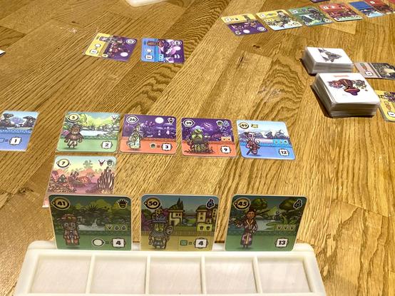 Faraway auf dem Fußboden. Man sieht die Handkarten eines Spielers und Teile seiner Auslage sowie die Auslage des Gegners. Nachziehstapel und „Markt“ sind in der Mitte zwischen den Spielern.