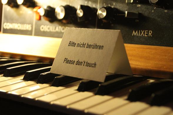 A small portion of a Moog Minimoog synthesizer, focusing on a small sign asking the visitor "Bitte nicht berühren – Please don't touch".