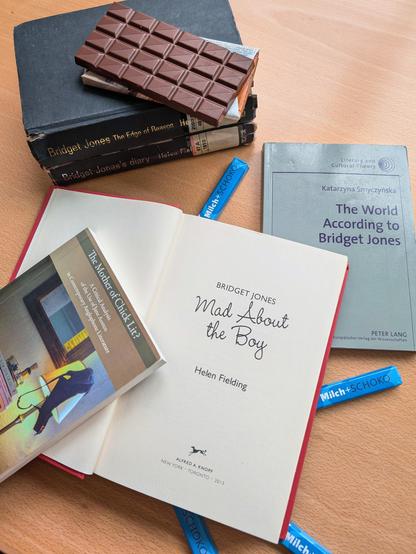 The first 3 Bridget Jones novels on a wooden table, as well as the 2 books "The World According to Bridget Jones" by 	Katarzyna Smyczyńska and "The Mother of Chick Lit?" by Julia Anna Wilhelm, surrounded by several chocolate bars