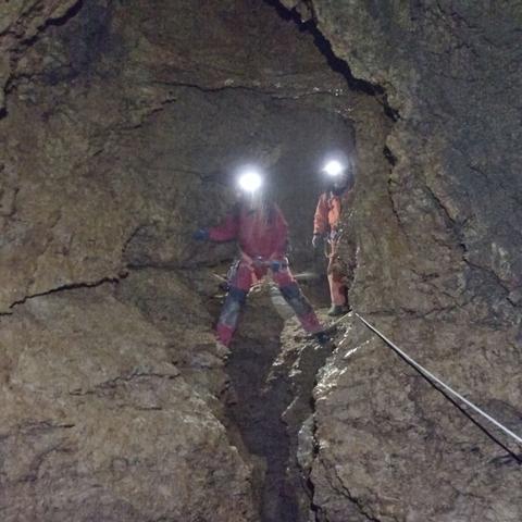 Two people in caving suits standing in a canyon looking into the camera.