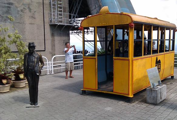 A statue standing in front of a yellow cable-car.