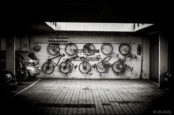 Garage. rechts und links Autos, An der hinteren Wand hängen 5 Fahrräder. Schwarz-Weiss Foto.