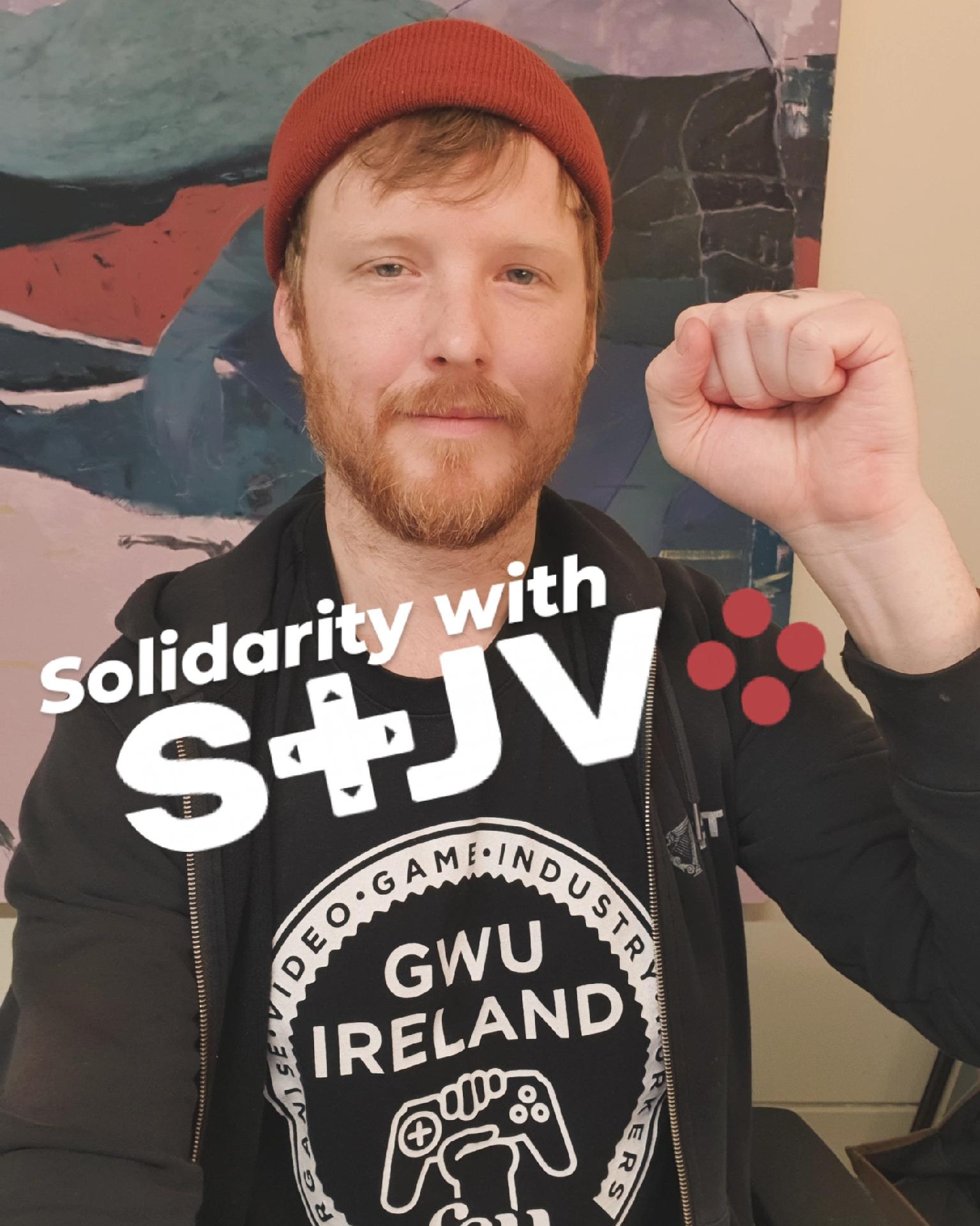 Denman holding a fist up in solidarity wearing a Game Workers Unite Ireland shirt. Text reads "Solidarity with STJV"