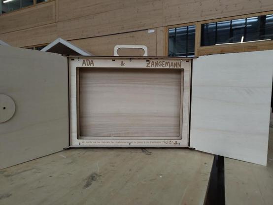 Opened front of the kamishibai. The text "Ada & Zangemann" is engraved on the top, above the hole for the pictures (no picture is present, we can see the back of the box). The inside of the doors is blank