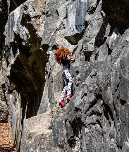 A Smart Doll with curly red hair, a black shirt and camo trousers climbing a rock.