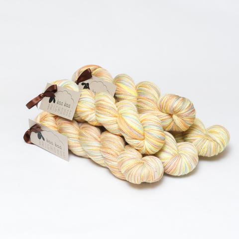 Picture shows a pyramid of five skeins of yarn positioned diagonally. The yarn is various shades of yellow, green, red, orange amd white.