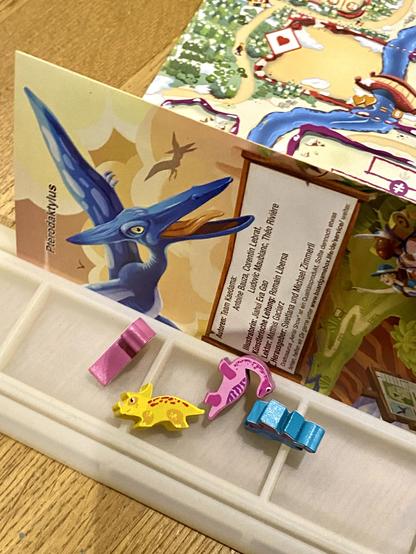 Nahaufnahme von einem Spielervorrat an Dinos mit dem Spielplan sichtbar im Hintergrund