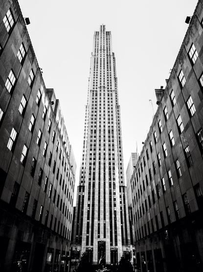 The Rockefeller Center seen between two rows of building, on a black and white photo.