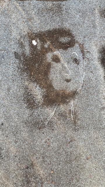 Ein Wasserfleck auf dem Boden, durch Kreide zu einem Gesicht ergänzt.