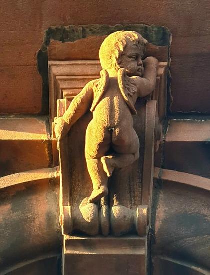 A sculpture of a mall, winged male baby climbing a keystone on a Glasgow building.