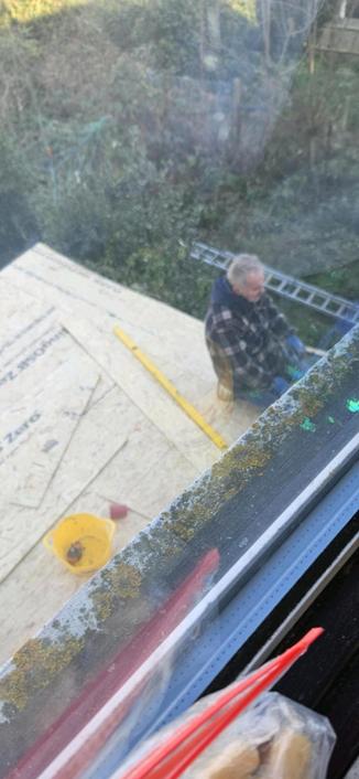A picture out of the window, you can see the new roof being installed and one of the roofing guys sitting on the edge of it singing.