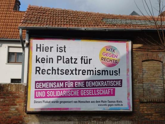 An einer Hauswand ein Plakat mit der Aufschrift "Hier ist kein Platz für Rechtsextremismus – Gemeinsam für eine demokratische und solidarische Gesellschaft.