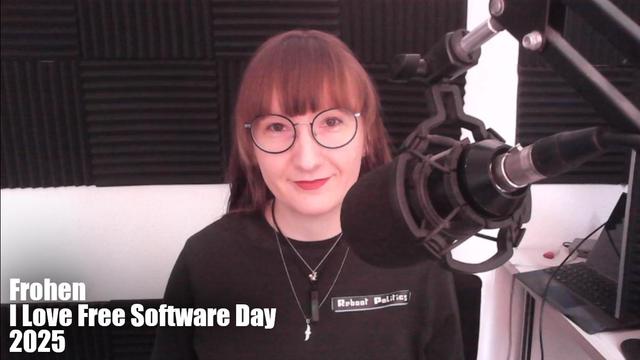 Ich, große Brille, rotbraune Ponyfrisur, blass, lächle in die Kamera und sitze an einem großen Mikrofon. Neben mir ist zu lesen: "Frohen I Love Free Software Day 2025".