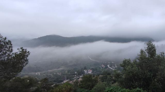 A cloud inversion layer above El Chorro village in Spain. Bushes in the foreground, houses below the cloud layer and the mountains the other side of the valley in the background with higher cloud above