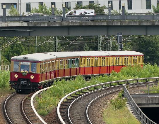 Historischer S-Bahnzug in einer Kurve, im Hintergrund eine Straßenbrücke über die Gleislandschaft