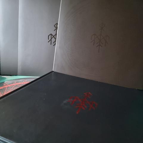 Taken out of the Box, the three Vinyl Gatefolds are actually housed in matte black O-card typed slip covers. These slipcovers only use UV varnish to print the band logo on the front and an individual runic circle artwork ont he back (not shown on the picture). Also included is a Vinyl slip mat. The book has the same makeup but instead of UV-varnish it uses red silverfoil printing.
