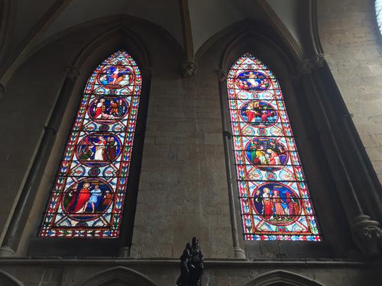 Two tall and narrow stained-glass windows with pointed arches, both very colorful and containing four roundels each. Each roundel depicts a biblical or hagiographical scene.