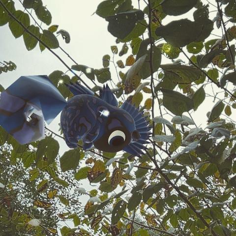 A dark blue and black Peridot creature hovering in the air in front of some leaves on a cloudy day.