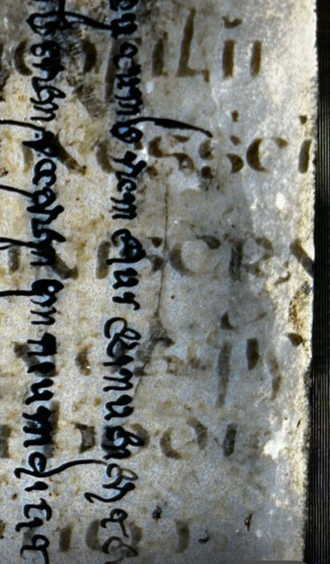 Part of a medieval manuscript, set on its side, with the two lines of the overtext in 2 vertical lines on the left, and 6 lines of faintly brown undertext running horizontally across the image.