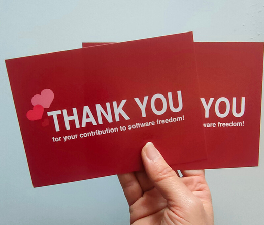 Hand holding two postal cards from the campaing I love Free Software Day. The cards are red with red hearts. They have the text: Thank You for your contribution to software freedom!