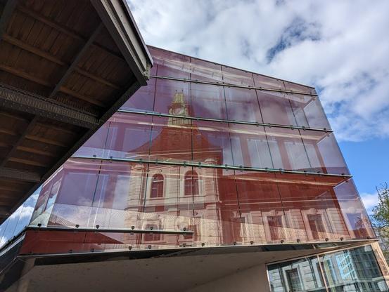 Photo of a building at Basel SBB, with the train station building reflecting in the glass front.