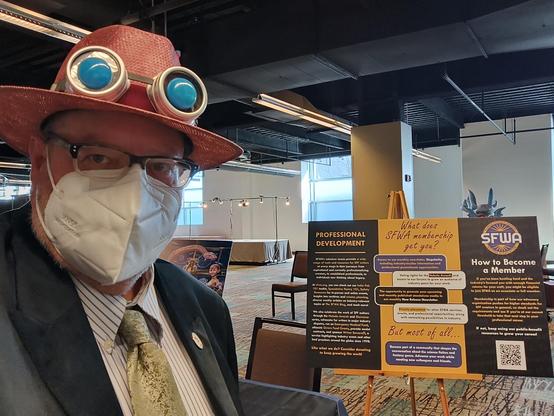 a well-dressed older man with a mask and steampunky hat standing in front of the SFWA signage