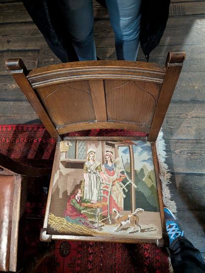 A chair with a cross-stitched seat featuring someone cross-stitching the seat of a chair.