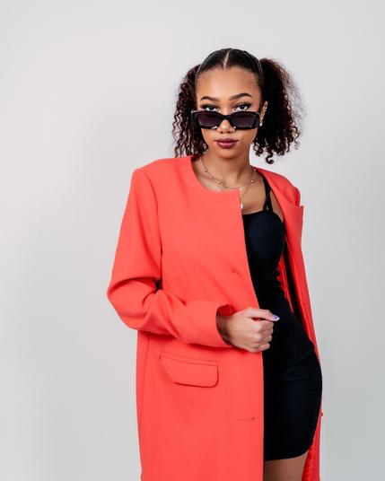 Young woman in a bold red coat and black dress, wearing stylish sunglasses, posing confidently in a photography studio in Lappeenranta.