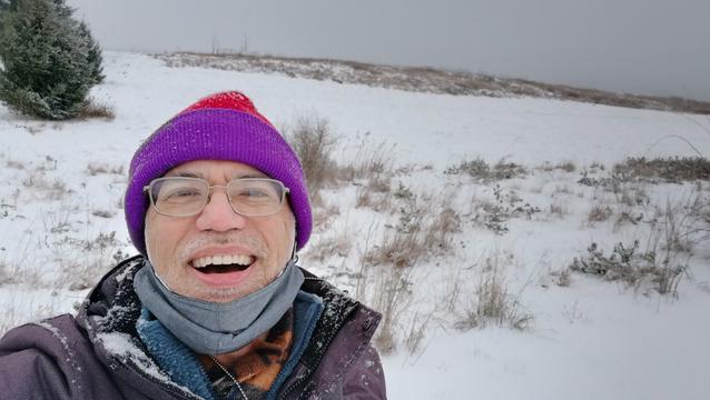 User JoeJoeTom in a selfie. He is dressed in winter gear including a cap, scarf, and jacket. He is standing in front of a snowy field.